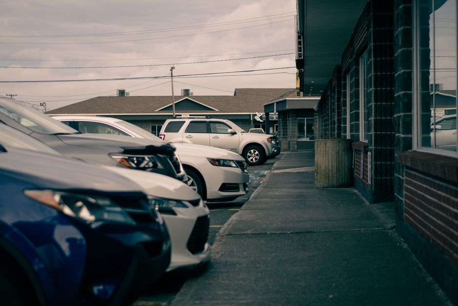 Row of contemporary automobiles parked against walkway and house facades under cloudy sky in town