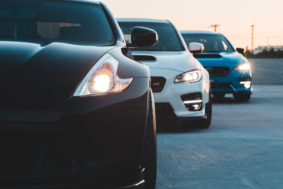 Contemporary sports cars with switched headlights parked in row at twilight