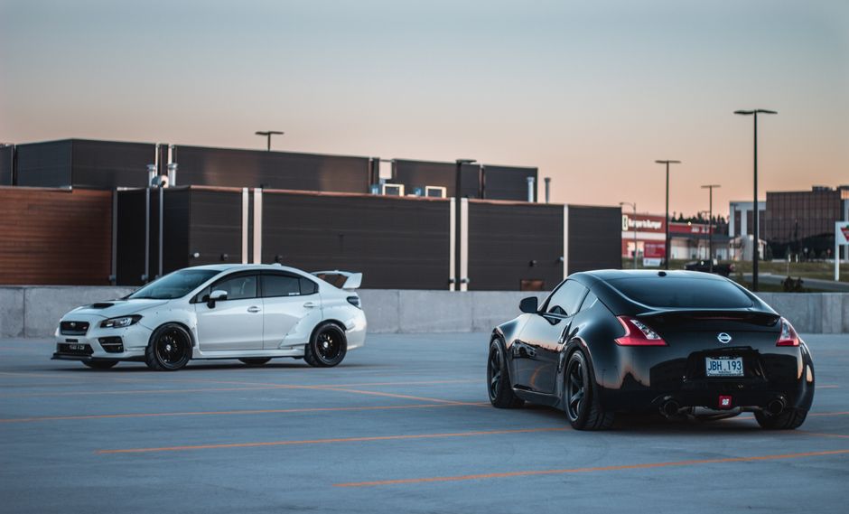Shiny various contemporary sports cars riding on parking area near modern building against cloudless sundown sky